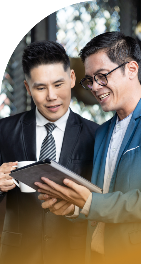 Two smiling businessmen in suits reviewing information on a tablet.